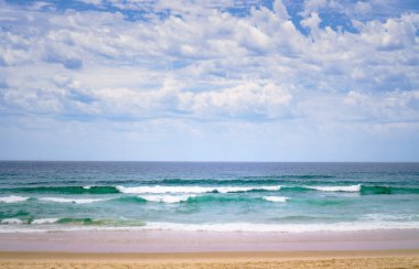 Okyanusun çarpıcı panoramik manzarası ve kumlu bir plajda yuvarlanan güzel dalgalar.