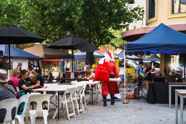 Gold Coast, Queensland, Avustralya - Aralık, 2018: Omzunda kırmızı bir çanta ile Noel Baba Zümrüt Göller pazarı yakınındaki sokakta kafede oturan insanlar geçen.