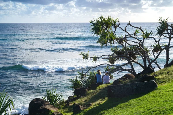 Gold Coast, Avustralya - Aralık,2018: Arkadaşlar okyanusa yakın tepede oturuyorlar ve gün doğumu sırasında kıyıya çarpan dalgaları izliyorlar.
