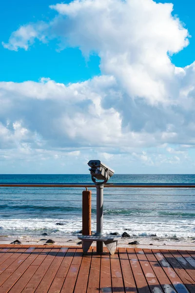 Altın Sahil teleskobu (deniz dürbünü) Pasifik Okyanusu'nun kenarındaki bir iskelede, önünde mavi bir gökyüzü arka planı üzerinde dalgalar ile duruyor. 