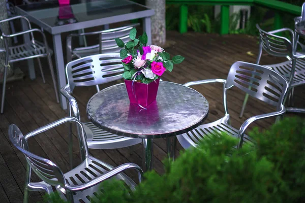 Vintage moody garden scene. Beautiful bouquet of white and pink roses in the pink vase standing on the metallic table in the green garden.