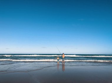Sörfçüler Cenneti plajının güzel geniş panoramik manzarası. Bir baba ve küçük oğlu Avustralya 'nın Gold Coast sahilinde balık tutuyorlar..