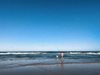Sörfçüler Cenneti plajının güzel geniş panoramik manzarası. Bir baba ve küçük oğlu Avustralya 'nın Gold Coast sahilinde balık tutuyorlar..