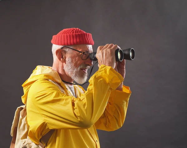 an Amazing man, a man in a red cap and a bright yellow raincoat enjoys the views of smortya in the distance using binoculars, isolated background. hobby