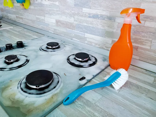 grey glass hob is covered with a cleaning foam from old dirt. house cleaning