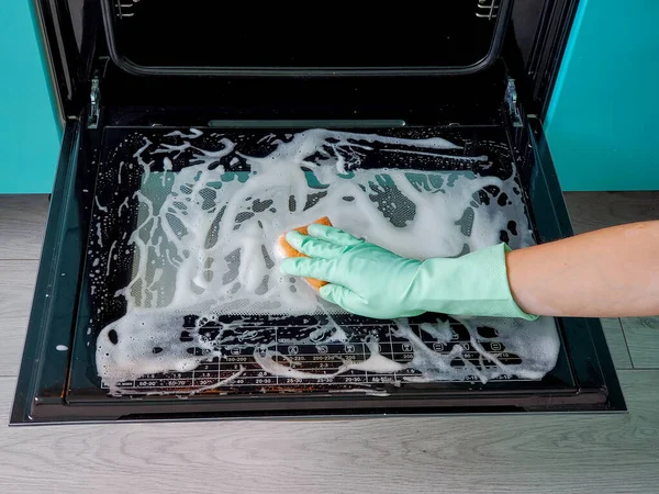 Close-up of a womans hand in rubber gloves washes the oven door