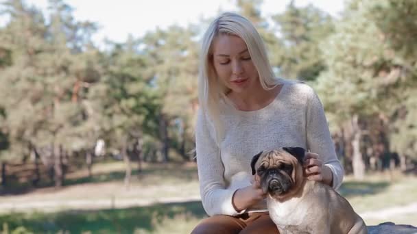 Біла жінка з pug, сидячи на камінь в парку — стокове відео