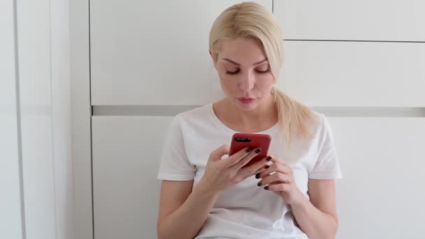 Молодая белая женщина с помощью смартфона, сидя на полу — стоковое видео