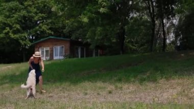 Bir köpekle oynayan sundress ve şapkalı kadın