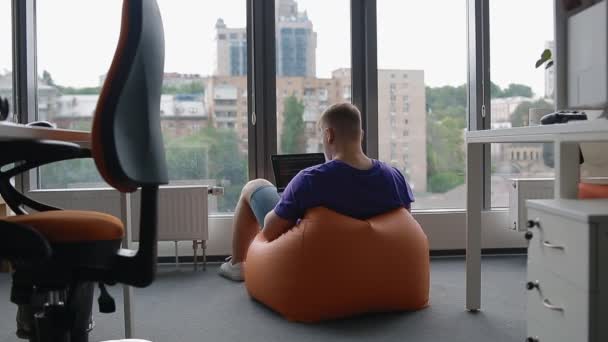 Young man working in modern office sitting on the sandbag — Stock Video