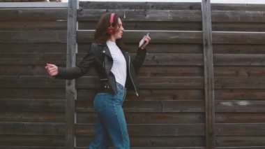 Genç kız duvarın önünde yürüyor müzik dinliyor ve dans ediyor.