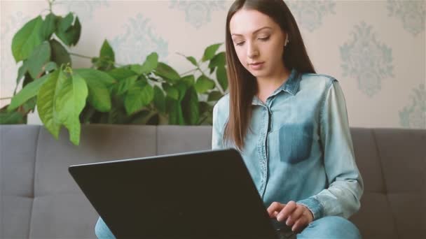 Ung kvinna skriva på laptop sitter på soffan hemma — Stockvideo