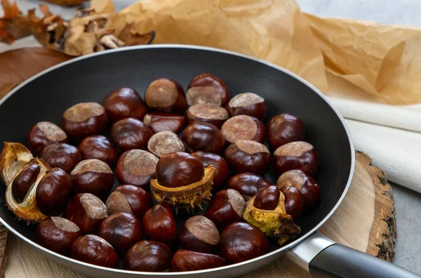 Taze, parlak kestaneler, sonbahar yaprakları ve kağıt paketlerle dolu bir tavada.