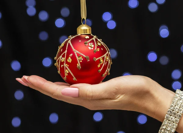 Mooie, sierlijke vrouwelijke hand houdt een indrukwekkende rode kerstbal — Stockfoto