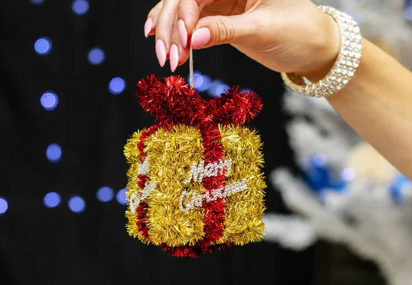 Girl holding a beautiful bright new year toy in the shape of a gift and the inscription merry christmas — Stock Photo, Image