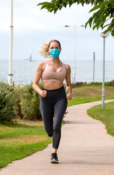 beautiful blonde woman runs in the park in a medical mask