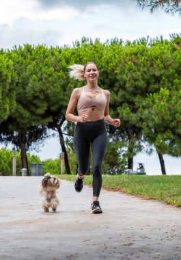 Güzel bir kız bir köpekle parkta koşuyor.