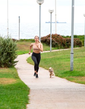 Güzel kız bir köpekle parkta koşuyor.