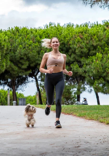 Güzel bir kız bir köpekle parkta koşuyor.