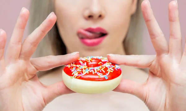 Adam taze donut tutar ve dudaklarını yalar. Pembe arka grubunda taze lezzetli donut kapağıyla.