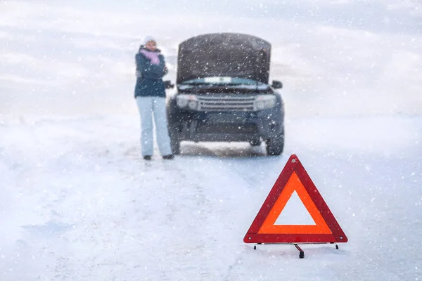 Uma mulher perto de uma máquina partida congela. À volta de um campo nevado. Sinal de emergência. Inverno . — Fotografia de Stock