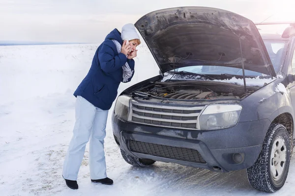 Bozuk arabaya bakan kadın motora bakıyor. Kış ve kar alanı çevresinde. — Stok fotoğraf