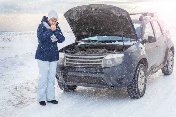 Mulher a olhar para o carro avariado a olhar para o motor. Em torno do inverno e campo de neve . — Fotografia de Stock