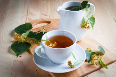 Bir fincan çay, çiçekler ve yapraklar ahşap bir masada..