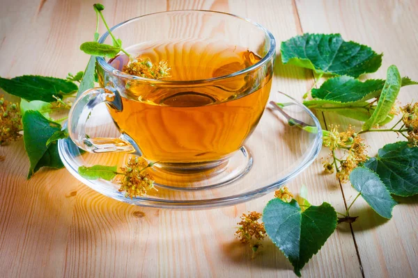 Чашка з чаєм, квітами і листям на дерев'яному столі . — стокове фото
