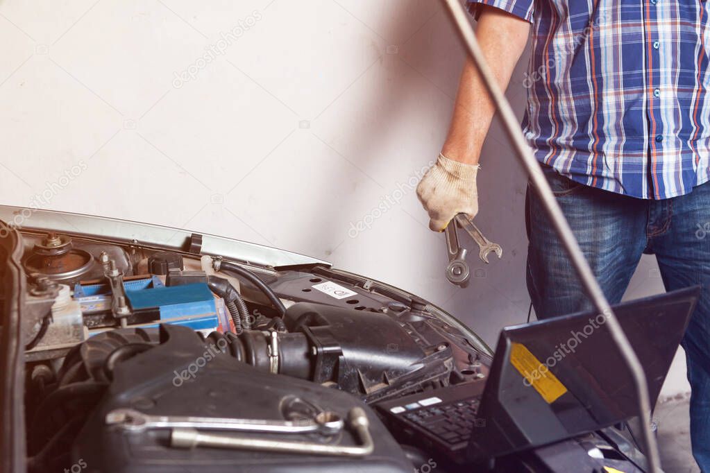 Car mechanic with a wrench in the garage doing car repairs.