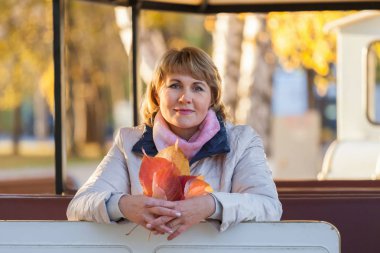 Orta yaşlı bir kadın sonbahar parkında ağaçların arasında yürüyor..
