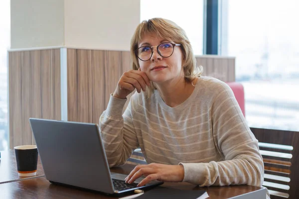 En kvinna på ett kafé som arbetar vid en dator vid fönstret. — Stockfoto