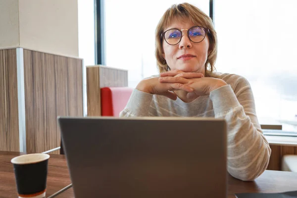 Una mujer en un café trabajando en una computadora en la ventana . — Foto de Stock