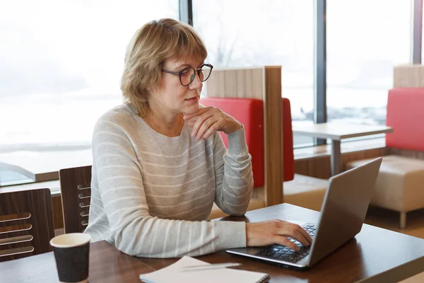 En kvinna på ett kafé som arbetar vid en dator vid fönstret. — Stockfoto