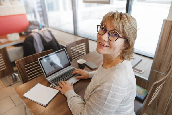 Una mujer en un café trabajando en una computadora en la ventana . — Foto de Stock