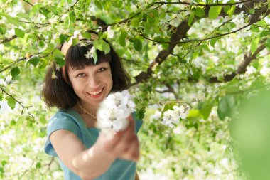 Bahar bahçesinde çiçek açan elma ağaçları olan uzun mavi elbiseli kadın.