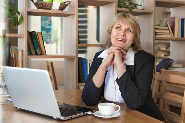 Женщина в белой рубашке с ноутбуком работает в кафе и в офисе — стоковое фото