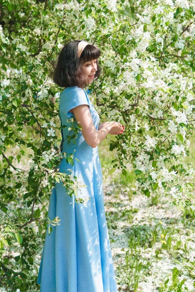 Kobieta w długiej niebieskiej sukience z kwitnącymi jabłoniami w wiosennym ogrodzie — Zdjęcie stockowe
