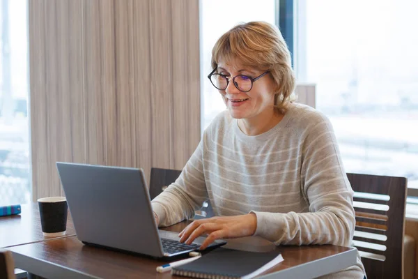 Uma mulher em uma camisa branca com um laptop trabalha em um café e no escritório — Fotografia de Stock