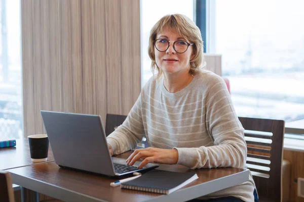 En kvinna i vit skjorta med laptop jobbar på kafé och kontor. — Stockfoto