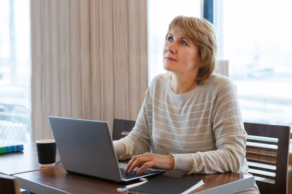 Uma mulher trabalha em um escritório e café com um laptop, ela tem um trabalho remoto — Fotografia de Stock