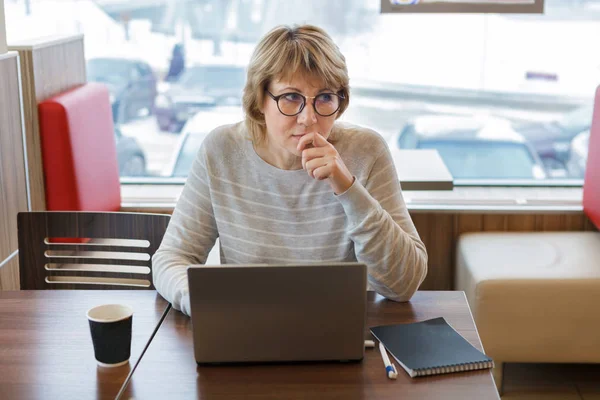 Женщина работает в офисе и кафе с ноутбуком, у нее есть удаленная работа — стоковое фото