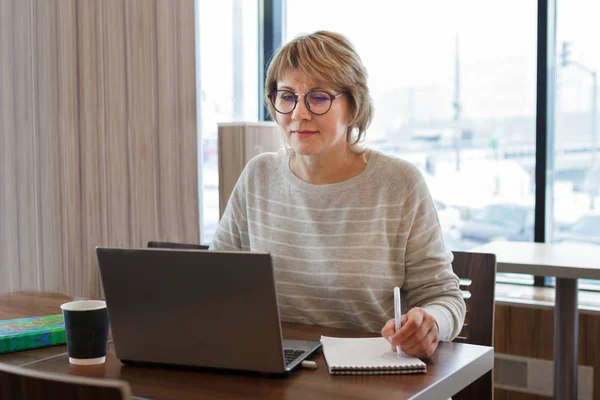 Uma mulher trabalha em um escritório e café com um laptop, ela tem um trabalho remoto — Fotografia de Stock