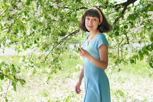 Dziewczyna w niebieskiej sukience stoi przy kwitnącym drzewie wiosną — Zdjęcie stockowe