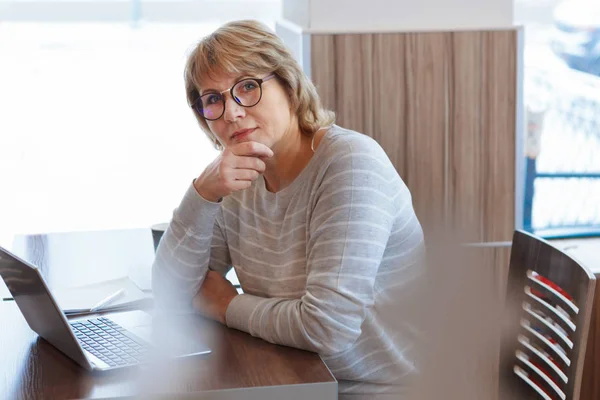 Mujer de mediana edad negocio en el lugar de trabajo en la cafetería, oficina, ella está trabajando en su computadora portátil . — Foto de Stock