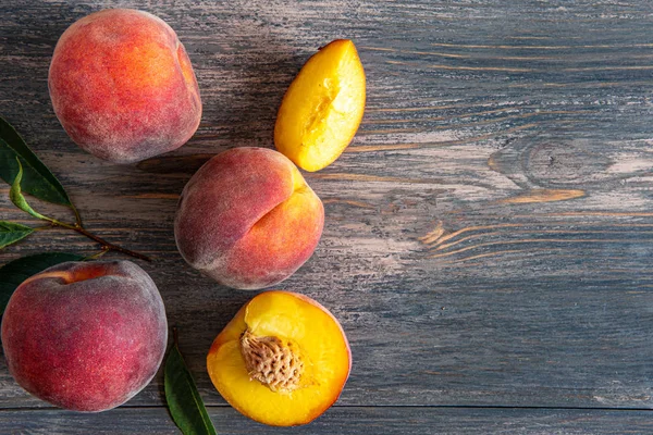 Sweet ripe juicy peaches with green leaves on a wooden background