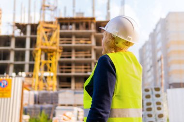 İnşaat alanındaki bir kadın inşaatçı tuğladan yapılmış bir evi inceliyor.