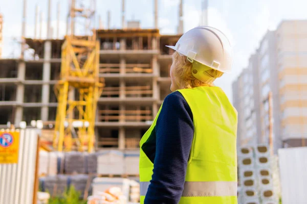 İnşaat alanındaki bir kadın inşaatçı tuğladan yapılmış bir evi inceliyor.