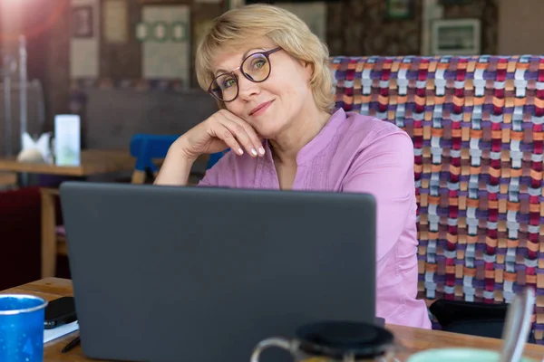 Una mujer con un portátil trabaja en un café en la oficina, es freelancer . — Foto de Stock