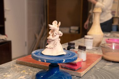 Bir kadın stüdyo atölyesinde kilden yapılmış seramik bir oyuncak yapıyor ve boyuyor..
